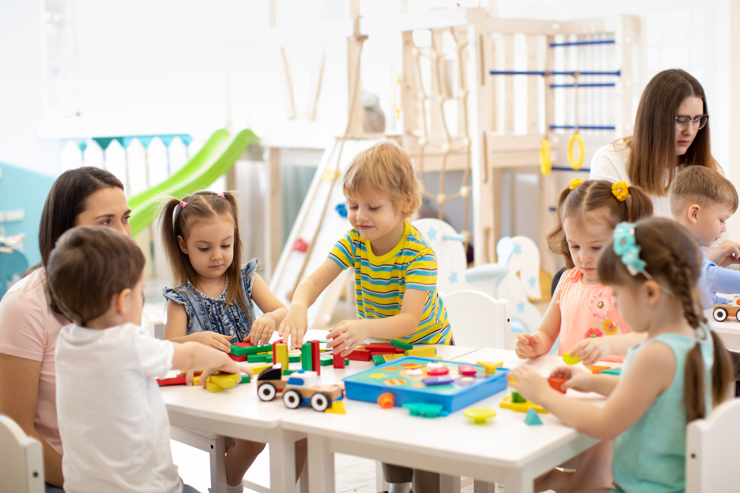 Kindergarten,Children,Playing,Toys,With,Teacher,In,Playroom,At,Preschool.